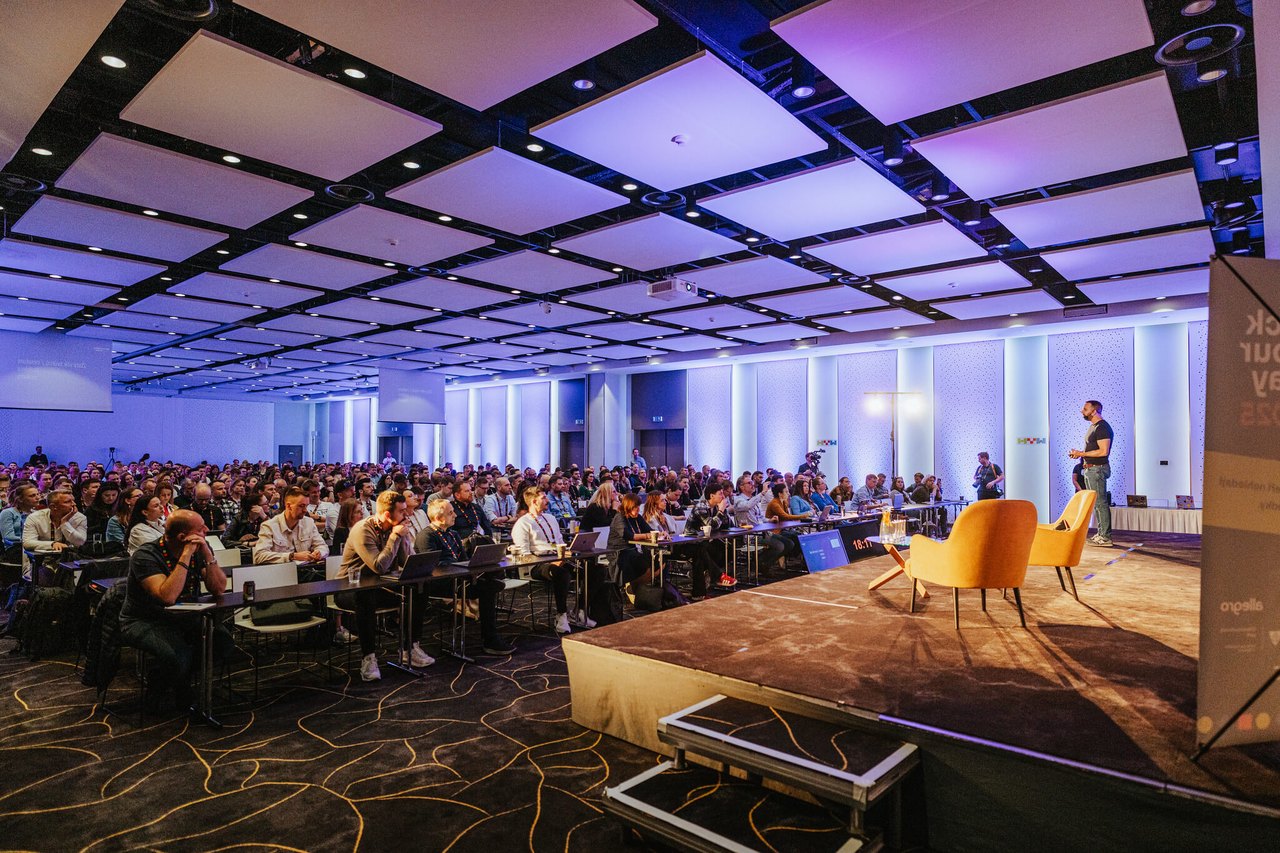 Konferenční sál Hack Your Way s publikem pod fialovým osvětlením